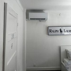 Een wandairco-installatie is zichtbaar, geplaatst in een moderne kamer met witte muren en minimalistische inrichting.
