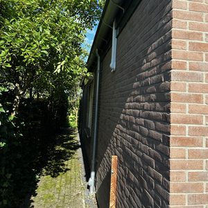 De foto toont een airco-installatie aan de buitenzijde van een woning, gedeeltelijk bedekt door bomen.