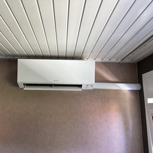 Moderne wand-airco-unit geïnstalleerd tegen een lichtgekleurde muur, met zichtbare leidingen.