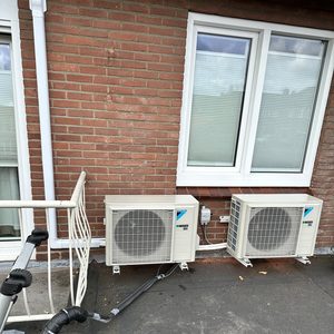Deze afbeelding toont een buitenunit van een airconditioningsysteem, geplaatst tegen een bakstenen muur.