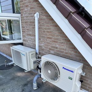 De afbeelding toont een buitenunit van een airconditioningsysteem gemonteerd op een plat dak, met leidingen die naar binnen leiden.