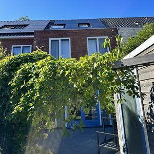 Een installatie van zonnepanelen op een schuin dak, met een helderblauwe lucht op de achtergrond.