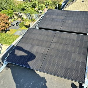 Twee zonnepanelen zijn geïnstalleerd op een schuin dak, met een uitzicht op een groene tuin.