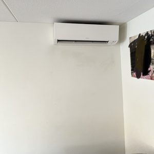De afbeelding toont een wandairconditioner gemonteerd aan de muur, bedoeld voor het koelen en verwarmen van binnenruimtes.