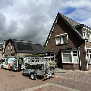 De afbeelding toont een woning met zonnepanelen op het dak, waar een installatieploeg aan het werk is.