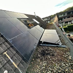 Een installatie van zonnepanelen op een hellend dak, met een werknemer die samenwerkt aan de opstelling.