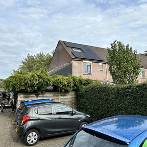 De afbeelding toont een woning met zonnepanelen op het dak, zichtbaar van een afstand. De installatie is geïntegreerd in de omgeving.