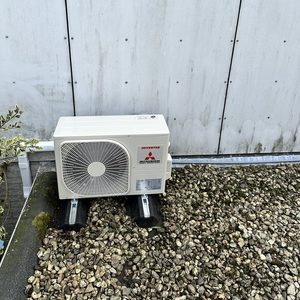 Installatie van een buitenunit van een airconditioningsysteem op een ondergrond van grind, voorzien van een kunststof afvoer.