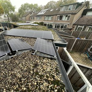 Deze installatie toont zonnepanelen bevestigd op een hellend dak, met een grindbedekking en diverse andere daken zichtbaar op de achtergrond.