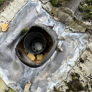 De afbeelding toont een gedeelte van een dak met een aansluiting voor zonnepanelen, omringd door verwering en mos.