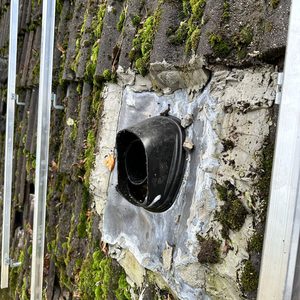 De afbeelding toont een deel van een zonnepaneleninstallatie met montagemateriaal op een dak, waaronder een bevestigingspunt en een doorvoer.