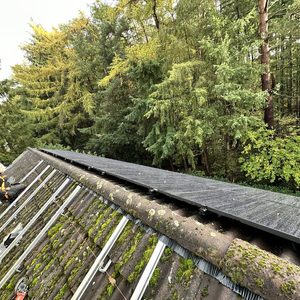 De foto toont een zonnepaneleninstallatie op een hellend dak, met een installateur die bezig is met de montage.
