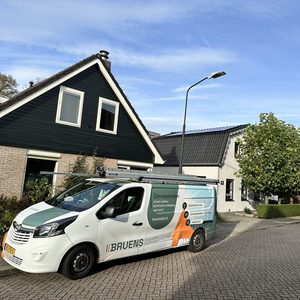 Een montagewagen staat geparkeerd voor een woning met zonnepanelen op het dak. De installatie is bezig of net afgerond.