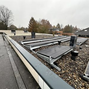 Deze installatie toont zonnepanelen die zijn bevestigd op een plat dak met grindbedekking.