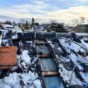 De afbeelding toont een gedeeltelijk geïnstalleerd zonnepaneelsysteem op een dak bedekt met sneeuw, met zichtbare rails en onderdelen.