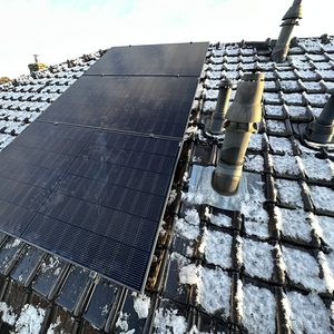 De foto toont een installatie van zonnepanelen op een schuin dak met sneeuwresten.