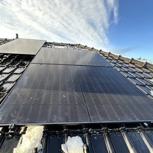 Een installatie van zonnepanelen op een hellend dak, zichtbaar zijn enkele panelen met een blauwe lucht op de achtergrond.