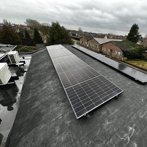 De installatie toont een reeks zonnepanelen op een plat dak, met een uitzicht op omliggende gebouwen en vegetatie.
