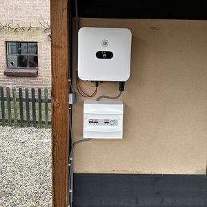 De afbeelding toont een omvormer die onderdeel is van een zonnepanelen-installatie, voorzien van bekabeling en een aansluiting voor netvoedsel.