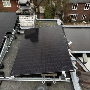 De installatie toont een zonnepaneel op een hellend dak, met montagemateriaal zichtbaar en een schoorsteen op de achtergrond.