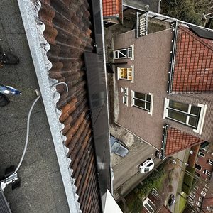 De foto toont zonnepanelen die zijn geïnstalleerd op een hellend dak, met een overzicht van de omliggende gebouwen.