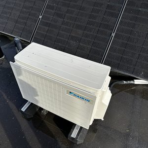 Een buitenunit van een Daikin airconditioningsysteem, geplaatst op een dak met zonnepanelen.