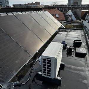 Een airconditioning installatie op een dak, met zonnepanelen op de achtergrond en verschillende aansluitingen zichtbaar.