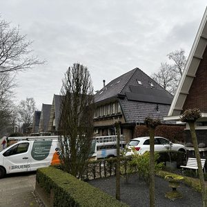 De afbeelding toont een woning met zonnepanelen op het dak, zichtbaar tussen bomen en andere gebouwen.