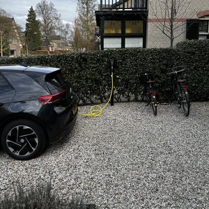 Een laadpaal voor elektrische voertuigen is in gebruik, met een auto ernaast en fietsen in de buurt.