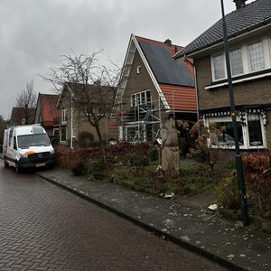 De foto toont een woning met zonnepanelen op het dak, tijdens een installatieproces met steigers zichtbaar.