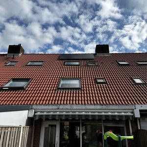 De foto toont een woning met zonnepanelen op het dak, deels in de schaduw van wolken.
