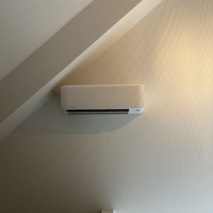 Een wandgemonteerde airconditioner geplaatst in een hoek met een schuin plafond.