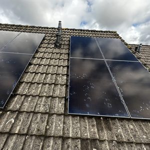 De installatie toont zonnepanelen op een schuin dak, met een duidelijke reflectie van de lucht op de panelen. Handafdrukken zijn zichtbaar op de panelen.