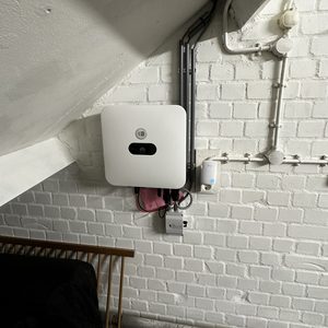 Installatie van een omvormer voor zonnepanelen, zichtbaar met bekabeling. Geplaatst aan een muur in een interieur.