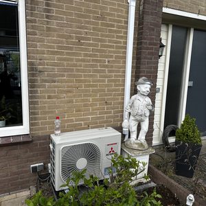 Een wandunit voor airconditioning is geïnstalleerd buiten, naast een huis. De unit heeft een inverter technologie.