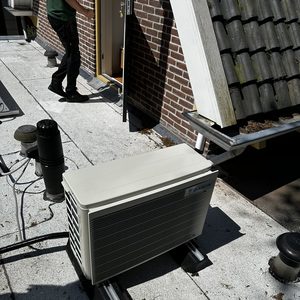 Een airco-unit wordt geïnstalleerd op een plat dak met toegang tot een deur.