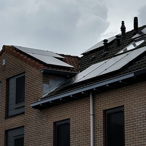 De afbeelding toont zonnepanelen geïnstalleerd op een hellend dak van een woning, met een grijze lucht op de achtergrond.