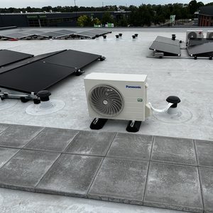 Een airconditioningseenheid op het dak, naast zonnepanelen, die koelcomfort biedt voor het gebouw.