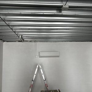 De afbeelding toont een airconditioning-installatie in een ruimte met zichtbare steiger en enkele materialen op de vloer.