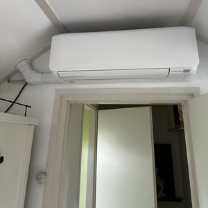 Een wandairconditioningseenheid geïnstalleerd in een interieur, met duidelijke leidingen zichtbaar.