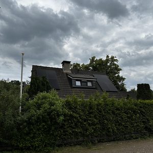 Deze fotovoltaïsche installatie met zonnepanelen ligt op het dak van een woning, omringd door groene begroeiing.
