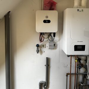 De afbeelding toont een omvormer voor zonnepanelen, met aansluitingen en een verbinding naar andere systemen in de ruimte.
