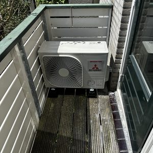 Een buitenunit van een airconditioninginstallatie, geplaatst op een balkon met houten planken.