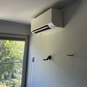 Een wandgemonteerde airconditioningseenheid geïnstalleerd in een kamer met uitzicht op groen.