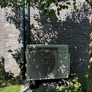 Deze installatie toont een buitenunit van een airconditioningsysteem, netjes geplaatst naast een muur met duidelijke zichtbare leidingen.
