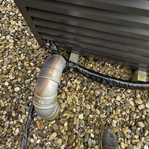 De afbeelding toont een deel van een installatie voor zonnepanelen, mogelijk een omvormer, met leidingen en bevestigingsmiddelen op een grindoppervlak.