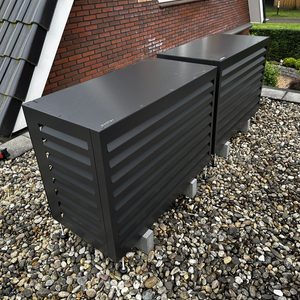 Twee zwarte thuisbatterijen zijn geplaatst op een gravelbed naast een woning, nabij de gevel.