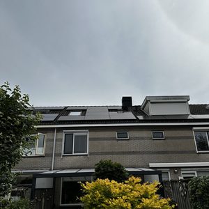 De foto toont een huis met zonnepanelen op het dak, geïnstalleerd naast een tuin met een boom en een overkapping.