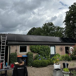 De afbeelding toont zonnepanelen die op een schuin dak zijn geïnstalleerd, met een persoon die aan het werk is in de nabijheid.