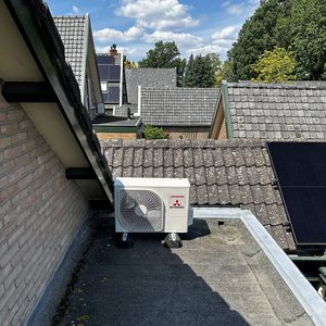De afbeelding toont een externe eenheid van een airconditioninginstallatie, geplaatst op een plat dak met zonnepanelen op de achtergrond.